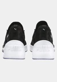 Mustat urheilukengät, joissa on pörröinen verkkomateriaali päällä ja valkoiset kumipohjat. Kenkien kantapäässä on kohdalleen tuotettu "PUMA"-logo ja muita logoelementtejä.