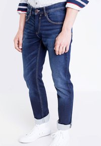 Mörkblå denimjeans med ljusa sömmar. Figursydd design, något avsmalnande ben och uppvikta fållar. Matchas med vita sneakers.