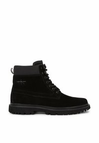 Stivaletto alla caviglia in suede nero con punta rotonda, suola in gomma e cuciture in tono. Presenta un colletto imbottito e un sistema di allacciatura con sei occhielli.