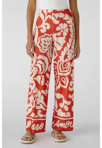 Spodnie typu wide-leg w jaskrawoczerwonym materiale z abstrakcyjnym białym wzorem paisley, z gładką teksturą i wyrazistym detalem w postaci pasa.