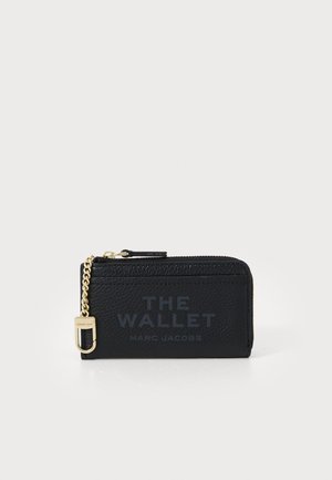 Svart lærpung med teksturert overflate, gullkjede som aksent og glidelås lukking. Har preget tekst "THE WALLET" og "MARC JACOBS."