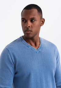 Suéter de v cuello azul claro, hecho de tejido de punto, con un cuello texturizado y puños acanalados, exhibido en un modelo sobre un fondo blanco.