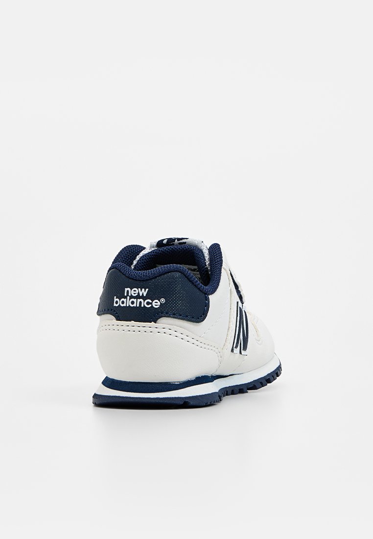 Baskets blanches avec des accents bleu marine, présentant un talon texturé, un logo surdimensionné et une semelle en caoutchouc avec un motif de semelle pour l'adhérence.
