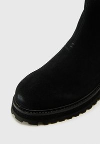 Botín negro de ante hasta el tobillo con punta redonda, parte superior texturizada y suela de goma gruesa con profundas versiones para tracción.