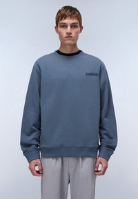 Light blue crewneck sweatshirt with ribbed cuffs and hem. Features a small, dark logo on the chest. Made from a smooth, soft fabric.