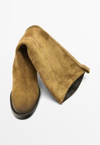 Stivaletti alla caviglia in pelle scamosciata marrone con una texture liscia, punta arrotondata e tacco basso a blocco, con un design a risvolto nella parte superiore.