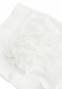 Calzino bianco fino alla coscia con un raffinato merletto decorativo lungo il bordo superiore, realizzato in un tessuto liscio e strutturato.