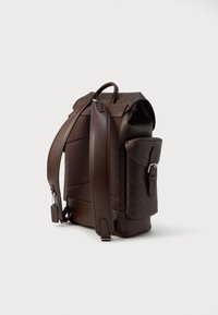 Zaino in cuoio marrone con una texture liscia e superficie decorata, dotato di spallacci imbottiti, una tasca laterale e dettagli in metallo robusti.