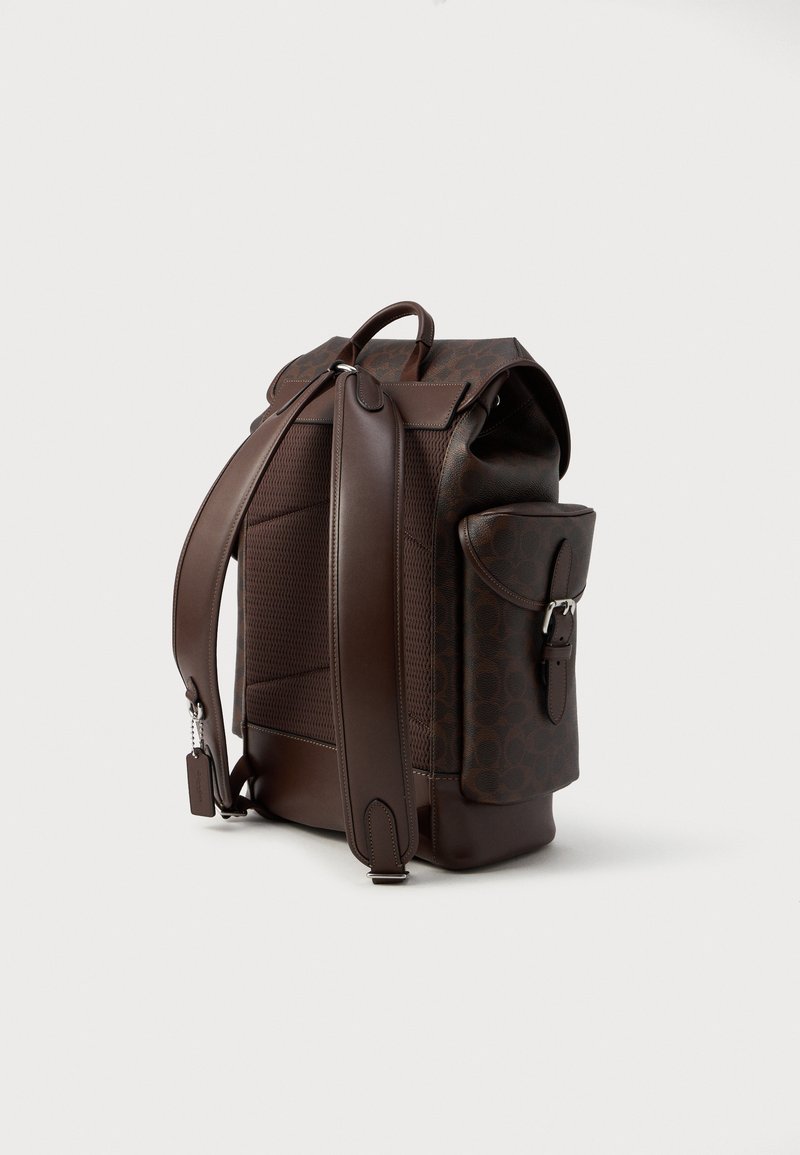Brown leather backpack with a smooth texture and patterned surface, featuring padded straps, a side pocket, and sturdy hardware accents.