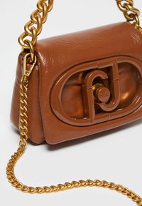Brown faux leather handbag with a gold chain strap, featuring a glossy emblem on the front and a compact, rectangular shape.