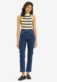 Sujetador de tirantes de canalé en crema con rayas negras, combinado con pantalones vaqueros rectos de tiro alto en azul oscuro y mocasines negros.