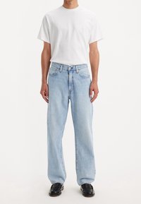 Ljust blå vida jeans i denim med en klassisk femfickdesign och knappgylf, kombinerat med en enkel vit T-shirt.