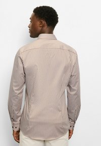 Braun-beiges, gestreiftes Langarmhemd mit Kragen, versehen mit knöpfbaren Manschetten und abgerundetem Saum. Glatte Stoffstruktur.