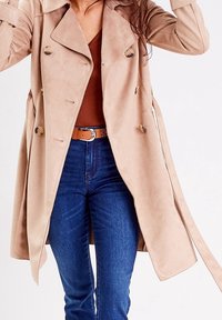 Beige trench coat z umělého semiše s dvouřadým zapínáním, velkými knoflíky a páskem na zavazování. Kombinováno s hnědým topem a modrými džíny.