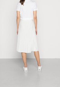 Bílá plisovaná midi sukně z lehkého materiálu, s rozšířeným lemem, kombinovaná s přiléhavým bílým topem a bílými teniskami.