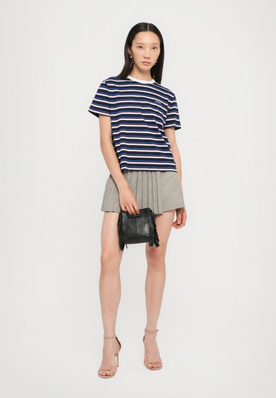 Marine gestreepte t-shirt met witte rand, geplooide grijze rok, zwarte handtas met franjes, en nude sandalen met bandjes.