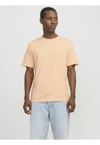 Camiseta de manga corta en color melocotón, hecha de algodón suave, con un cuello redondo y un corte relajado. Se lleva con jeans de mezclilla azul claros.