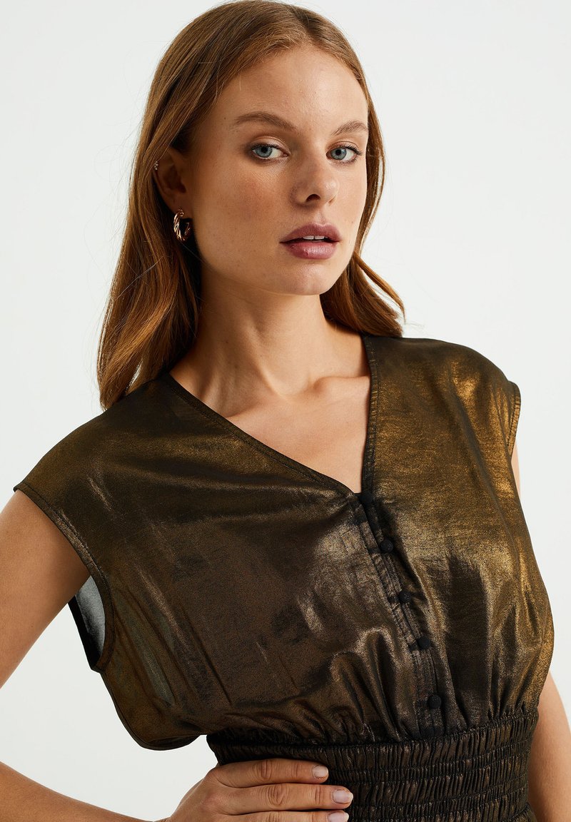 Bronzen metalen top met een v-hals, korte mouwen en knoopdetail. Heeft een gathered elastische taille en een zachte textuur.