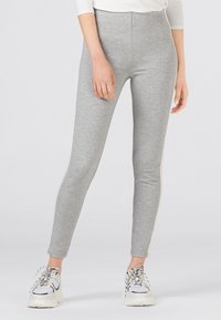Grå leggings av mjukt material, med en åtsittande design och hög midja samt minimala sidodetaljer. Bärs med vita sneakers.