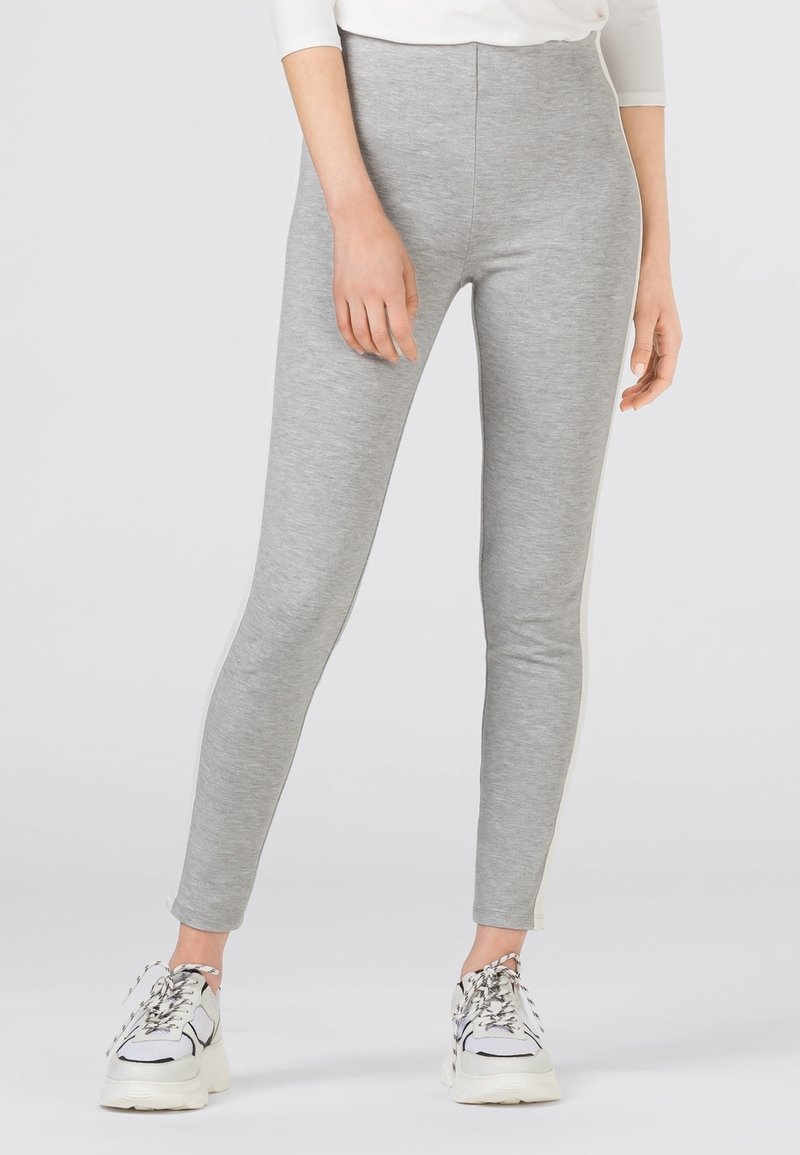 Grå leggings av mjukt material, med en åtsittande design och hög midja samt minimala sidodetaljer. Bärs med vita sneakers.