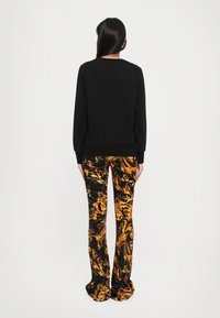 Čierna mikina s guľatým výstrihom, skombinovaná s nohavicami so zlatým a čiernym vzorom s vírivým dizajnom a rozšíreným strihom.
