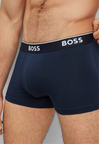 Nachtblaue Boxershorts mit einem weißen und schwarzen Bund, der den Markennamen "BOSS" enthält. Glatte Stoffoberfläche und enganliegendes Design.