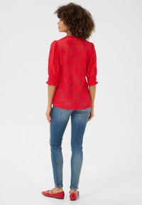 Červená krajková blůza s nařasenými rukávy, květinový vzor, poloprůhledná textura. Kombinováno s modrými skinny džíny a červenými balerínami.