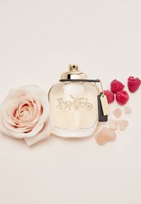 Klar glassparfymeflaske med gullkapsel, gravert design av en hestevogn, ledsaget av en lys rosa rose og bringebær.