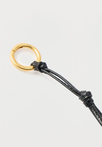 Μαύρο λουράκι από δέρμα με λεία υφή, που διαθέτει χρυσό μεταλλικό δαχτυλίδι με γυαλιστερό φινίρισμα, προσαρτημένο σε μία άκρη με λεπτομέρεια κόμπου.