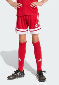 Shorts de sport rouges avec des rayures blanches et le logo Adidas, portés avec des chaussettes montantes rouges dotées d'accents de logo blancs, le tout associé à des crampons de football noirs.