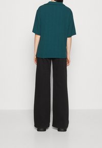 Teal ribbad kortärmad skjorta med krage, kombinerad med svarta vida byxor. Outfitten har ett texturerat tyg och en avslappnad passform.