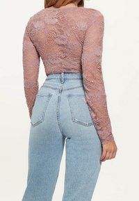 Lace Langarmtop in Mauve mit Blumenmuster, kombiniert mit hochtaillierten hellblauen Jeans im klassischen Fünf-Taschen-Design.