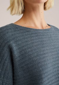 Gestrickter Pullover aus weichem, strukturiertem Stoff. Hat einen runden Halsausschnitt und dezent horizontale Streifen in einem gedämpften Blau-Grau.