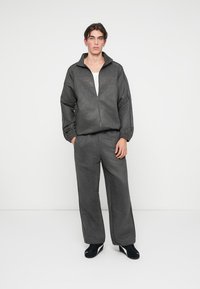 Casaco cinza escuro com fecho de correr e punhos elásticos, combinado com calças largas a condizer. Tecido suave e texturizado, sem padrões ou elementos metálicos visíveis.