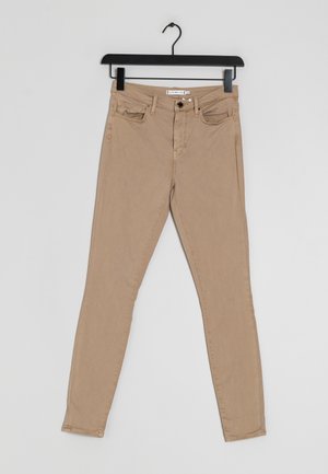 Beige slim-fit pants with front button and zipper, five pockets, hanging on a black hanger against a white background.