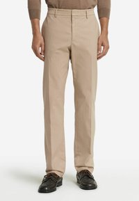 Beige skräddarsydda byxor med rak benform, med platt front och bälteshällor, matchade med mörka snörskor.