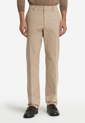 Pantaloni beige su misura con taglio dritto, caratterizzati da una parte frontale piatta e passanti per cintura, abbinati a scarpe stringate scure.