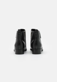 Czarne skórzane botki za kostkę o gładkim wykończeniu, z bocznymi zamkami i niskim układanym obcasem. Minimalistyczny design, bez widocznych wzorów czy ozdób.