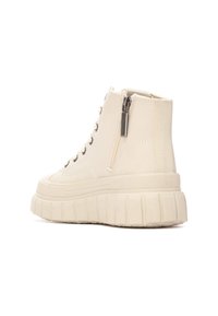 Zapatillas altas de color crema con una parte superior texturizada, cierre de cremallera en el lateral y suela gruesa con estrías para mayor altura.