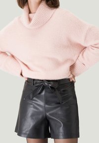 Helles rosa, gemütliches Wollrollkragenpullover kombiniert mit hochtaillierten schwarzen Ledershorts, die ein gebundenes Schleifendetail an der Taille aufweisen.