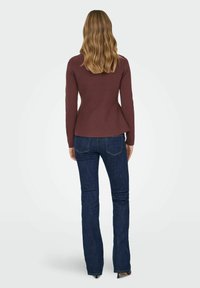 Bordeauxrotes, figurbetontes Langarmshirt mit ausgestelltem Saum, kombiniert mit dunkelblauen ausgestellten Jeans. Glatter Stoff und minimale Nähte.