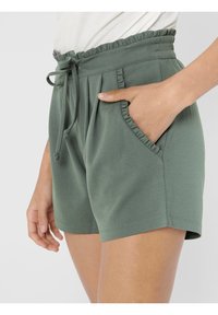 Zelené šortky vyrobené z měkké tkaniny, s nabíraným pasem, šňůrkou na stažení a šikmými kapsami. Hladká textura s volným střihem.