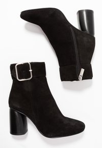 Botas de tobillo de ante negro con punta afilada, tacón grueso, cremallera lateral y un puño que presenta un gran diseño de hebilla plateada.