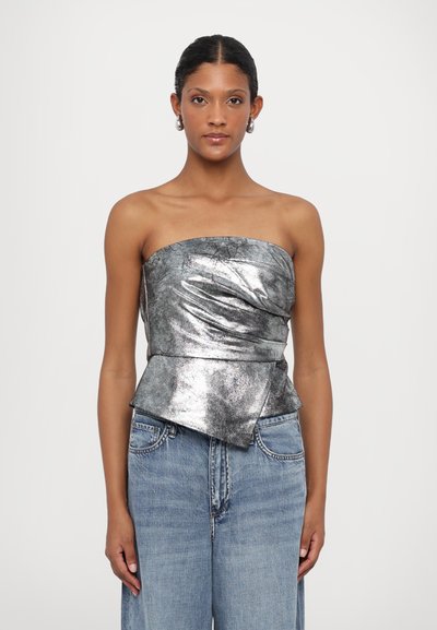 Metallisch silbernes trägerloses Oberteil mit taillierter Passform und Peplum-Saum, kombiniert mit hellblauen weit geschnittenen Jeans. Glatte Textur und strukturiertes Design.