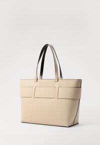 Borsa tote beige con una texture liscia, dotata di due manici neri robusti, una forma strutturata e tre tasche frontali rettangolari.