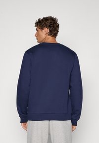 Granatowy sweter wykonany z gładkiego materiału, z żebrowanym okrągłym dekoltem i mankietami, o luźnym kroju, bez widocznych logotypów czy wzorów.