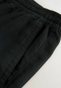 Black, elastic waist pants with a textured fabric, featuring side pockets and stitched detailing along the seams. Compact and functional design.