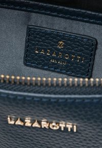 Dunkelblaues Lederetikett mit geprägt "LAZAROTTI" in Gold, mit strukturiertem Oberflächen und einem subtilen Stofffutter samt sichtbarem Reißverschluss.
