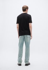 Μαύρο T-shirt με κοντά μανίκια συνδυασμένο με ανοιχτό μπλε, φαρδιά τζιν και μαύρα παπούτσια, που φαίνεται από πίσω σε ουδέτερο φόντο.