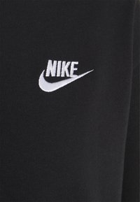 Black cotton t-shirt featuring white embroidered Nike logo and swoosh on the left chest. Smooth texture, fitted design.